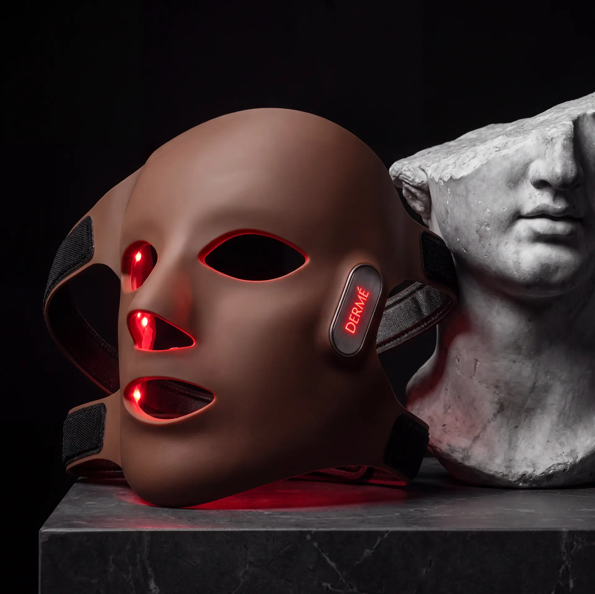 Dermé G11 laser mask lit red beside a classical marble bust